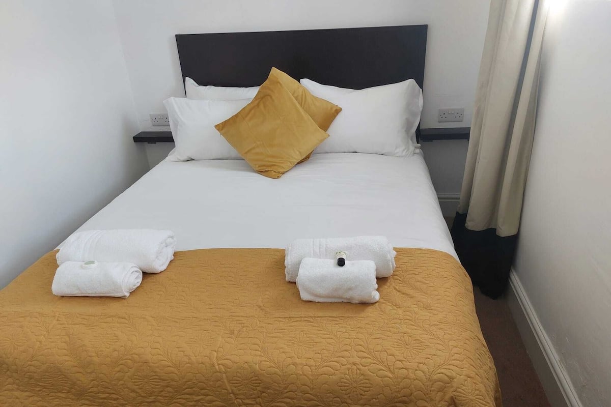 A hotel room with a bed, two white towels, a mustard-colored bedspread, and a black headboard.