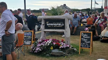 Un groupe de personnes s’est rassemblé autour d’une enseigne indiquant « The Springfield Bar & Restaurant », avec un tableau noir servant de menu.