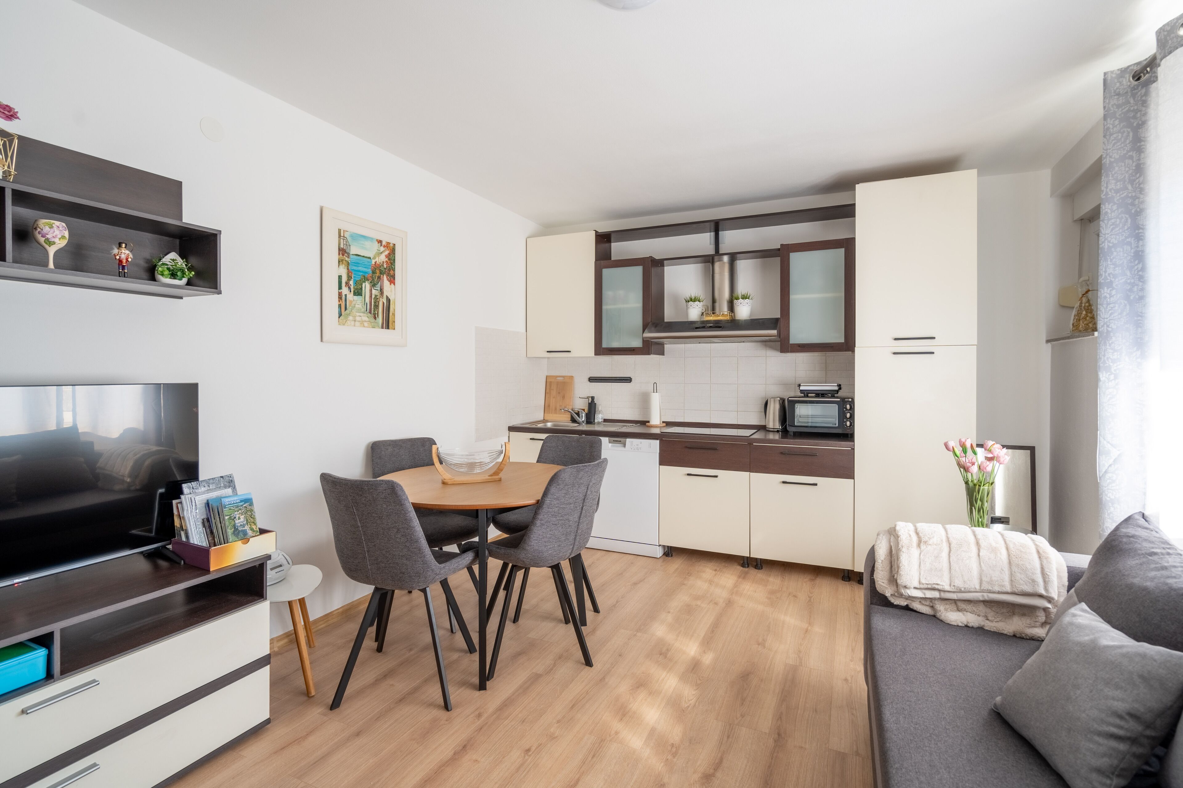 A modern apartment with a dining area, kitchenette, and a living room with a sofa and TV.