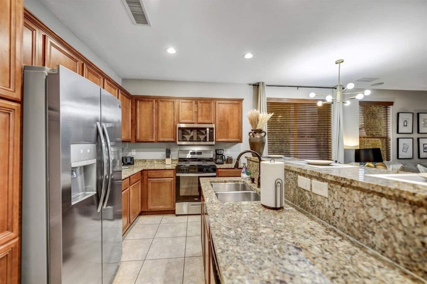 A modern kitchen with wooden cabinets, stainless steel appliances, granite countertops, and a large window with blinds.