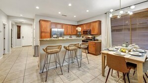 A modern kitchen with wooden cabinets, a stainless steel refrigerator, and a dining area with a table set for four.