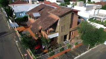 Vista aérea de um edifício com telhado inclinado, varanda visível e um pequeno jardim.