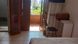A hotel room with a bed, a desk, a chair, a TV, and a balcony with a view of buildings and greenery. - Merlyn Pousadas (Lajeado)