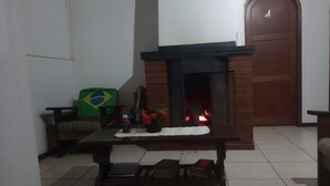 A room with a tiled floor, a fireplace with visible fire, a sofa with a Brazilian flag, and a wooden door marked with the number 4. - Merlyn Pousadas (Lajeado)