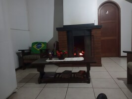 Um quarto com piso de azulejos, lareira com fogo à mostra, sofá com bandeira do Brasil e porta de madeira com o número 4.