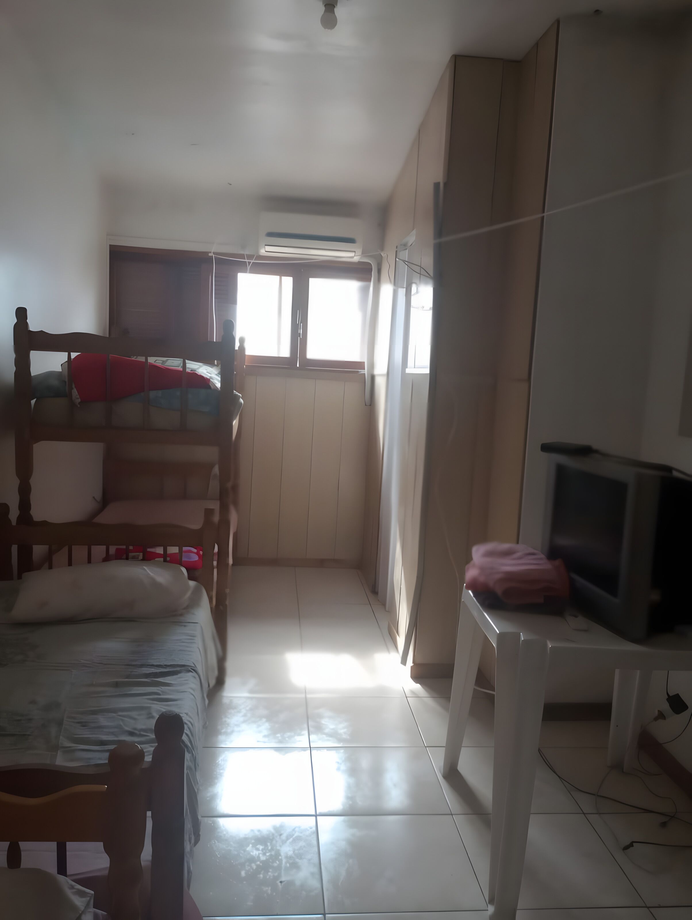Ein Zimmer mit Etagenbett, Schreibtisch und Fernseher, sowie einem Fenster für Tageslicht.