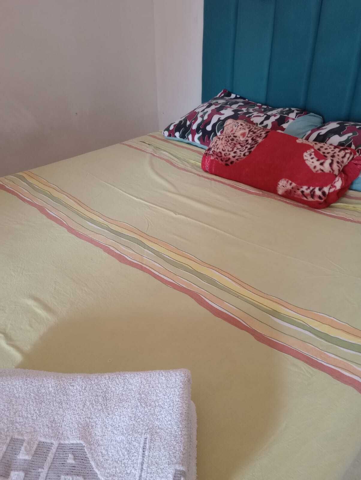 Una cama con una colcha a rayas y una almohada roja.