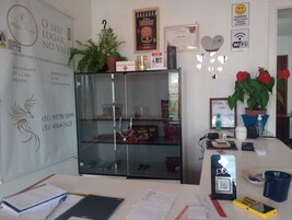 Uma receção com divisória de vidro, uma planta em vaso, um certificado emoldurado e um código QR para o registo.