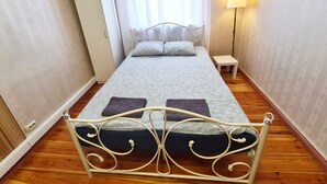 Un dormitorio ordenado con estructura metálica en la cama, una mesita de noche, una lámpara y un armario.