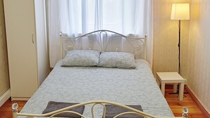 Un dormitorio con cama, armario, mesita de noche, lámpara y un cuadro en la pared.