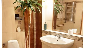 Un baño con inodoro, lavamanos y espejo. Hay una planta en maceta cerca del inodoro.