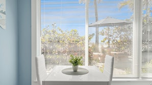 A dining table with a potted plant, white chairs, and a view through white blinds to the outdoors. - Charming Beach Front Studio Steps to the Sand and Gulf (Longboat Key)