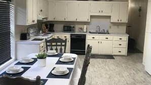 A compact kitchen with white cabinets, a dining table set for four, and a ceiling fan.