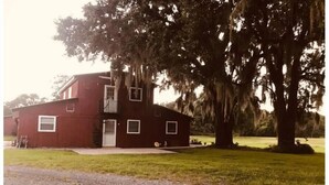 A two-story red building with a small porch and a large tree with hanging moss.