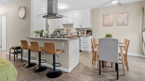 Una cocina moderna con una isla central, taburetes de bar y un comedor con sillas de madera.