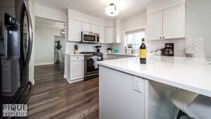 A modern kitchen with white cabinetry, a central island, and a stainless steel refrigerator. - 6B Luxury Home - Patio✔AC✔King Bed☆Park - WiFi (Edmonton)