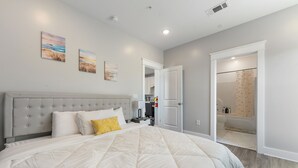 A bedroom with a large bed, a grey headboard, and two paintings on the wall.
