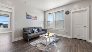 A living room with a gray sofa, a white coffee table, and a large window with blinds.