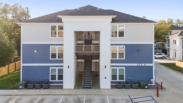 A two-story building with a central staircase, a parking area with trash bins, and a sign indicating a handicapped parking space.