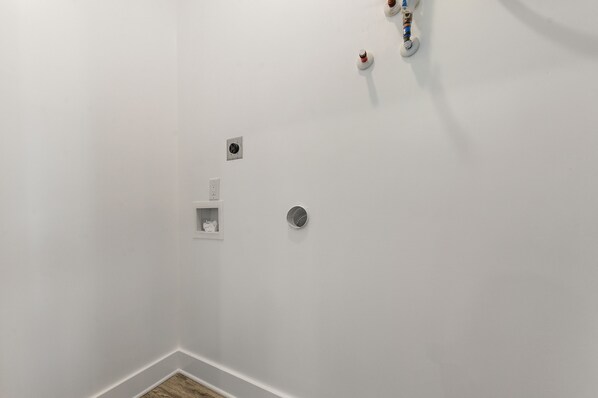 A white-walled room with a corner vent, a small shelf with a decorative item, and a round vent on the wall.