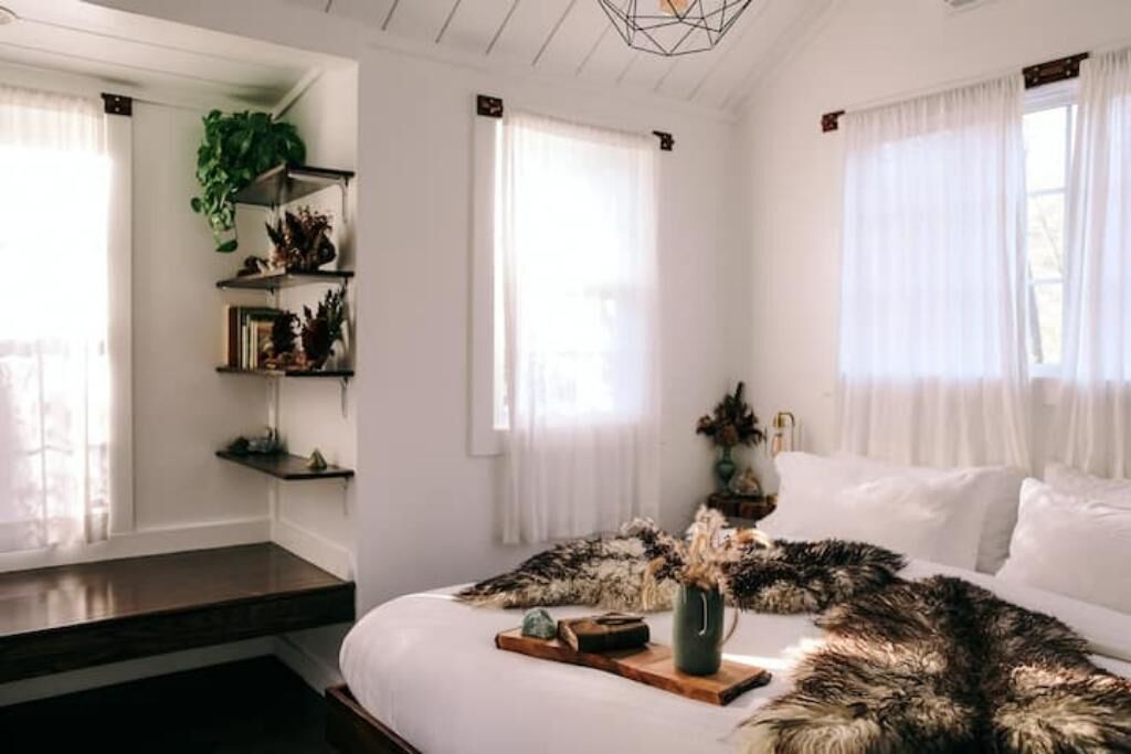 Une chambre avec un grand lit, un banc en bois et une plante posée sur une étagère.
