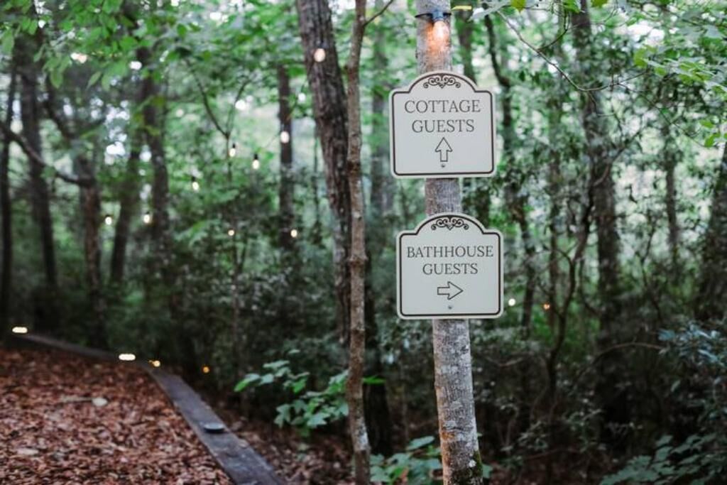 Un cartello in una zona boschiva con frecce direzionali che indicano 'COTTAGE GUESTS' e 'BATHHOUSE GUESTS'.
