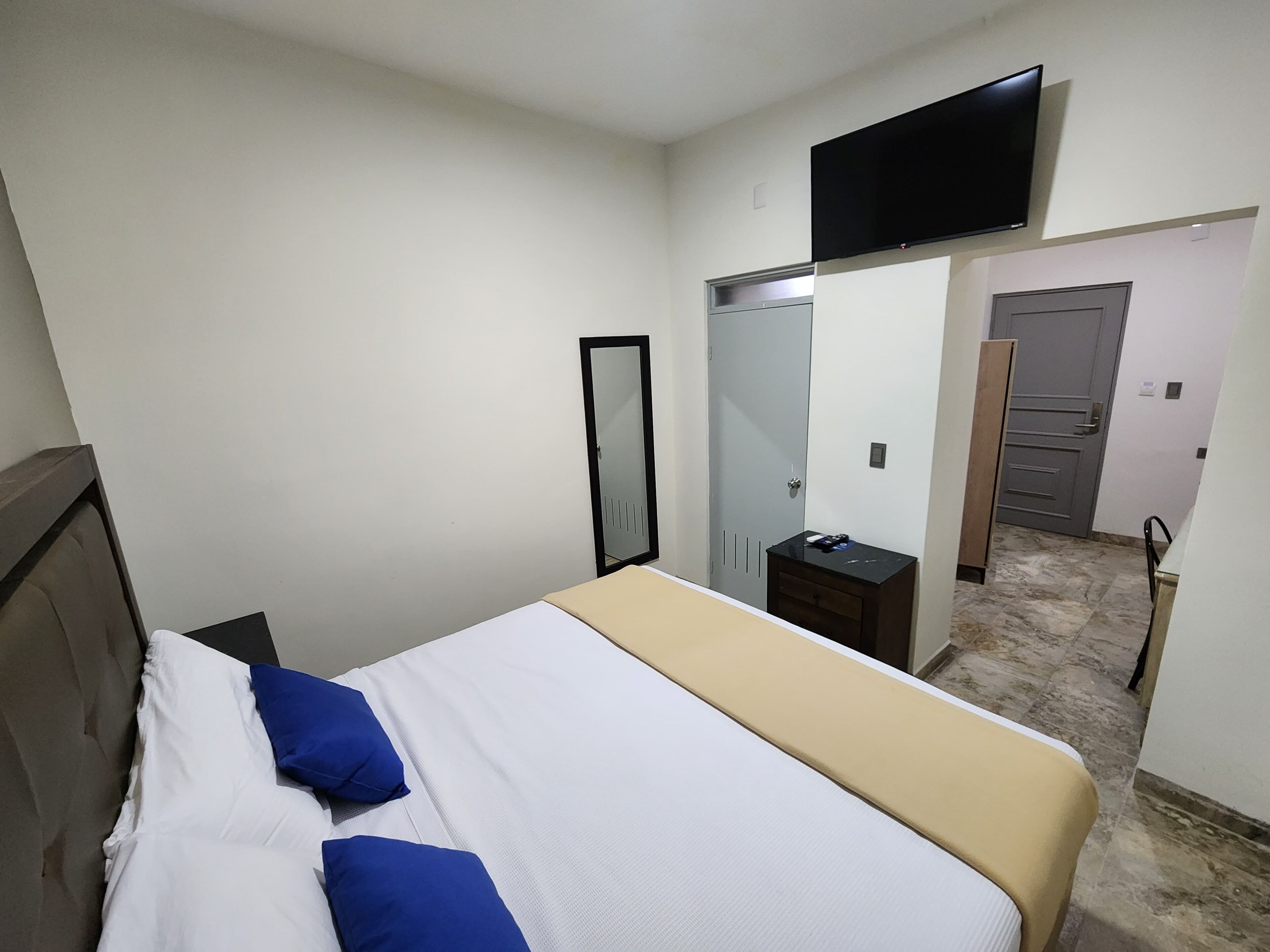 Ein Hotelzimmer mit einem Bett, einem an der Wand montierten Fernseher, einem Spiegel, einem Kleiderschrank und einer Tür zu einem Badezimmer.