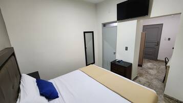 Ein Hotelzimmer mit einem Bett, einem an der Wand montierten Fernseher, einem Spiegel, einem Kleiderschrank und einer Tür zu einem Badezimmer.