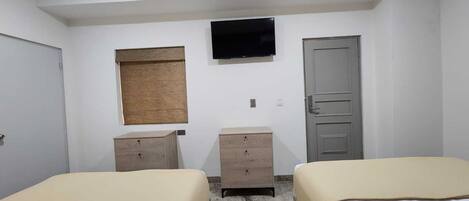 A small, clean room with two beds, a television, a window, and a door.