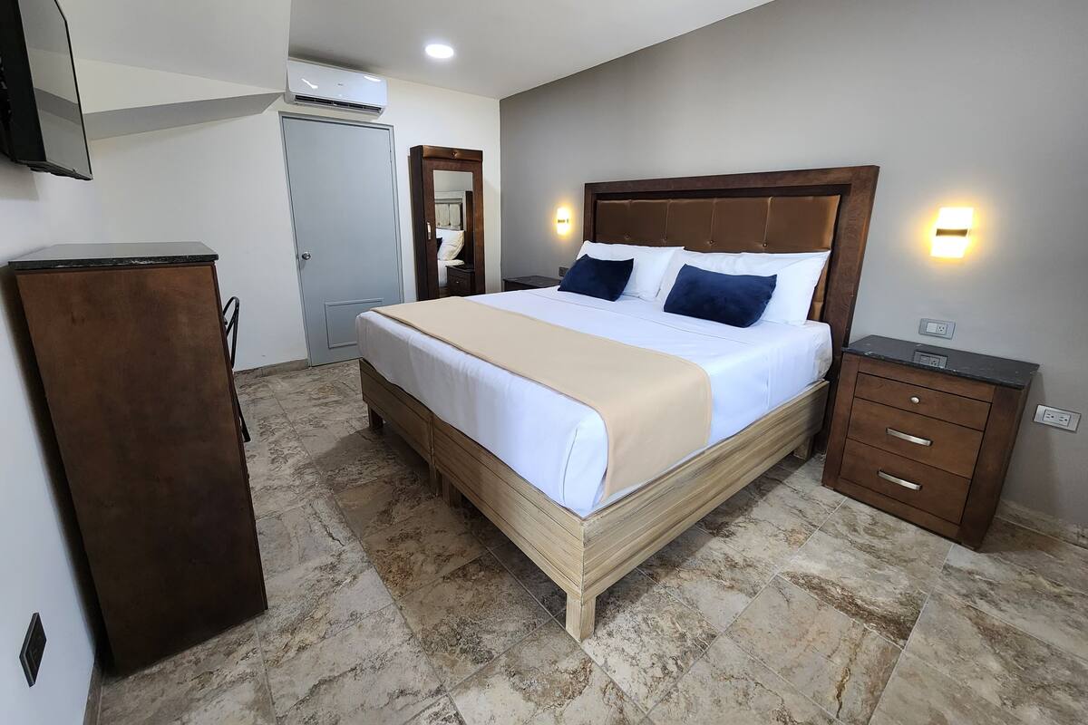 A neatly arranged bedroom with a large bed, bedside tables, a wardrobe, and an air conditioning unit.