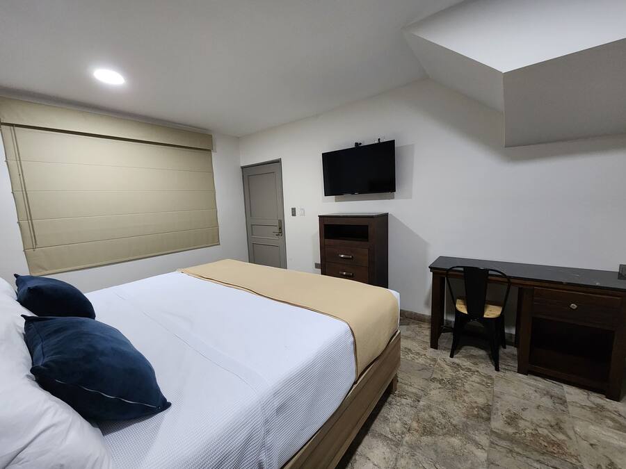 Quarto com cama, escrivaninha, cadeira, televisão e guarda-roupa.