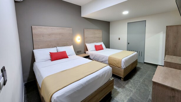 A hotel room with two beds, a wardrobe, a desk, and a wall-mounted air conditioner. - Hotel Roque (Torreón)