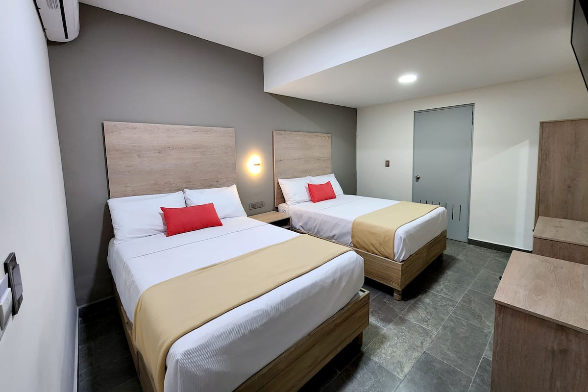 A hotel room with two beds, a wardrobe, a desk, and a wall-mounted air conditioner.