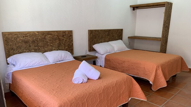 Deux lits simples avec des têtes de lit marron, des oreillers blancs et des couvre-lits orange, dans une pièce dont le sol est recouvert de carreaux.