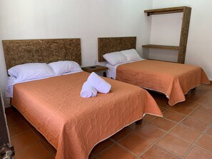 Dos camas individuales con cabeceros marrones, almohadas blancas y colchas naranjas en una habitación con suelo de baldosas.