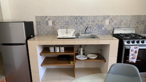 Une cuisine compacte équipée d’un réfrigérateur, d’une cuisinière et d’un plan de travail recouvert de carreaux.