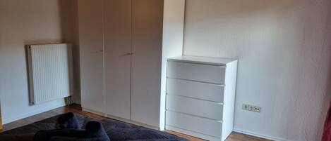A bedroom with a bed, a radiator, a wardrobe, and a shelving unit.