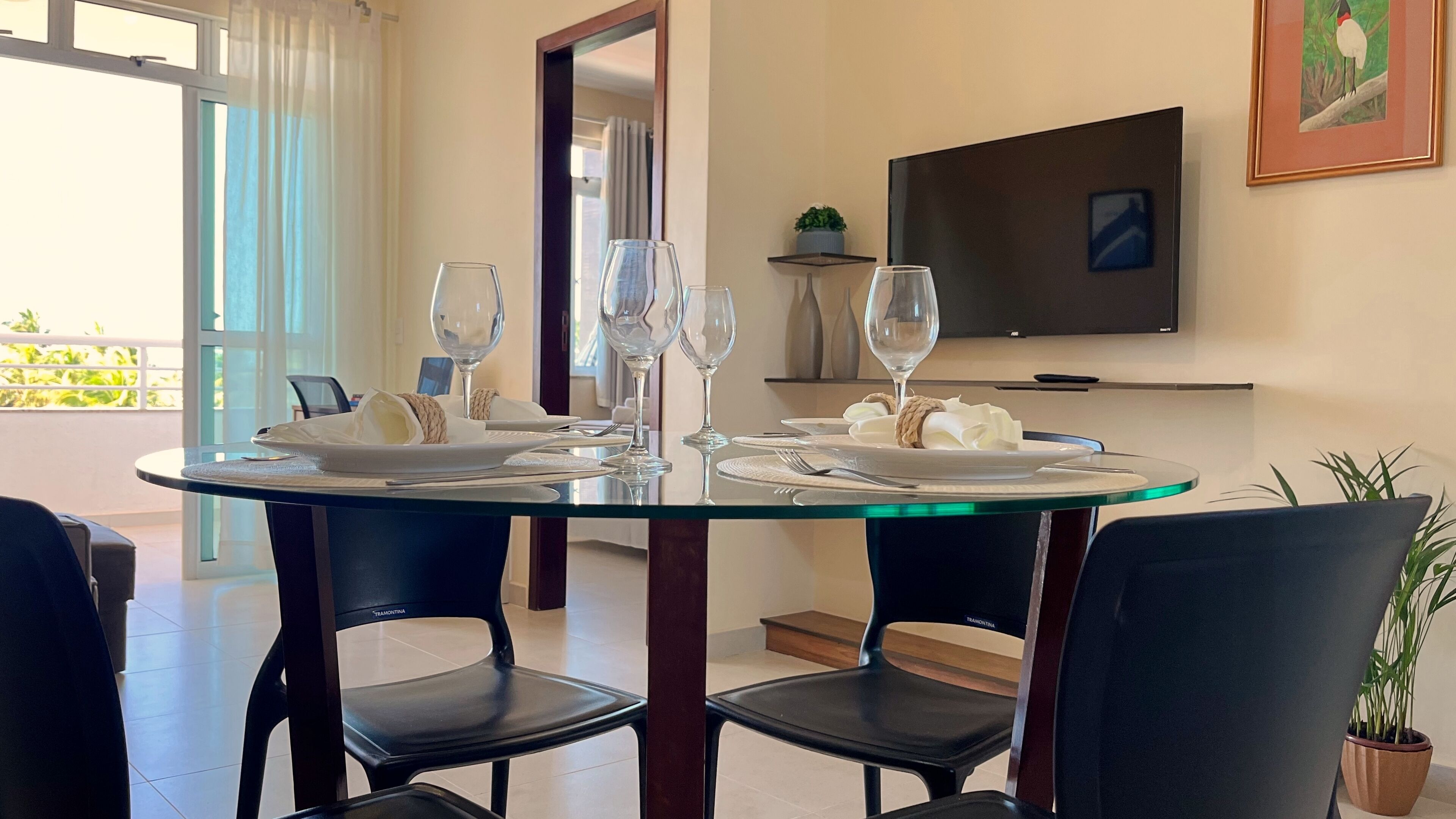A dining area with a glass table, black chairs, and a TV mounted on the wall.