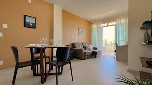 A dining area with a table set for four, a sofa, and a balcony with curtains. - 2 suítes ideal p/ amigos e casais (Aquiraz)