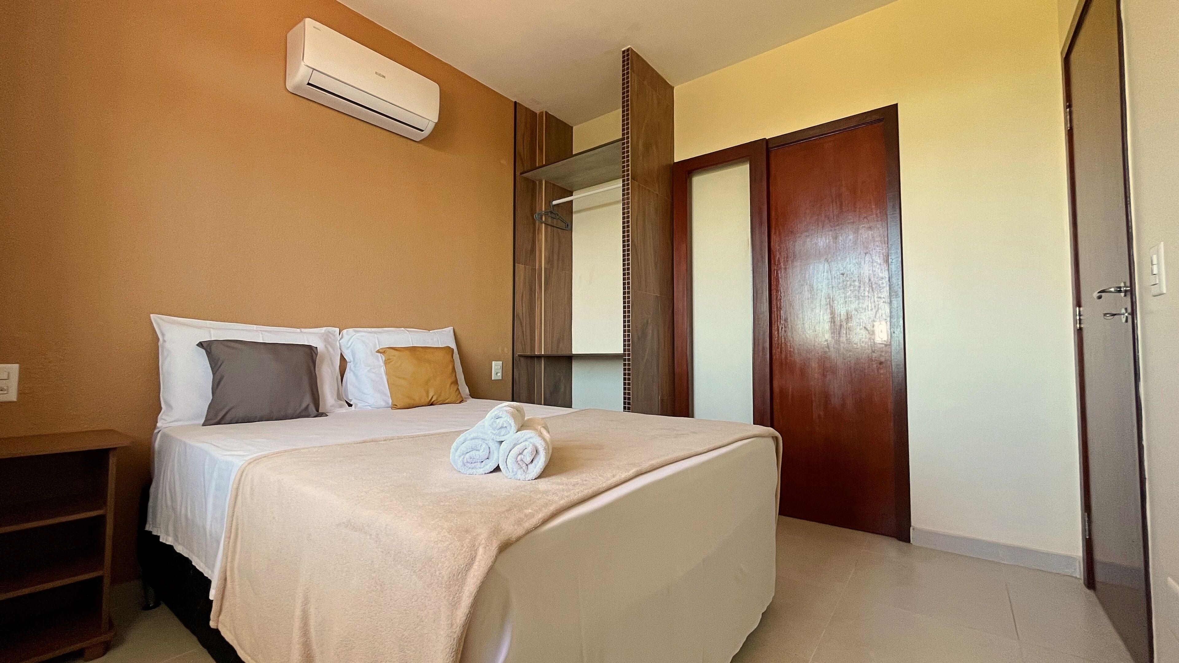 Quarto de hotel com cama, guarda-roupa, unidade de ar condicionado e porta de banheiro.