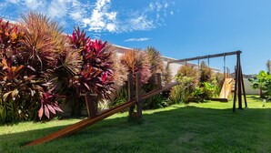 A backyard with a swing set, lush green grass, and various plants. - 2 suítes ideal p/ amigos e casais (Aquiraz)