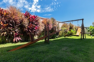 Un patio trasero con un columpio, césped verde exuberante y diversas plantas.