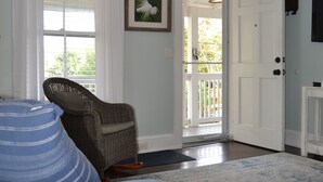 Ein Zimmer mit Deckenventilator, einer weißen Tür, einem Korbstuhl, einem blauen Sofa und einem gemusterten Teppich.
