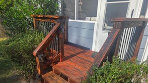 Une terrasse en bois avec des marches menant à une porte, le tout entouré de verdure.