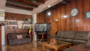 A cozy living room with wooden walls, a sofa, a coffee table, a TV, and a bookshelf. - Casa Hotel Sura (San José)