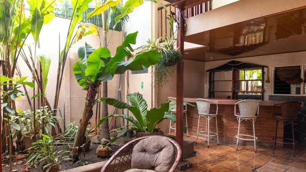An indoor patio with wicker chairs, a glass table, and various potted plants. - Casa Hotel Sura (San José)