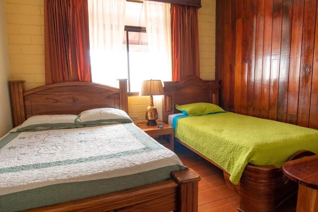A room with a wooden bed, a bedside table with a lamp, and a green blanket.
