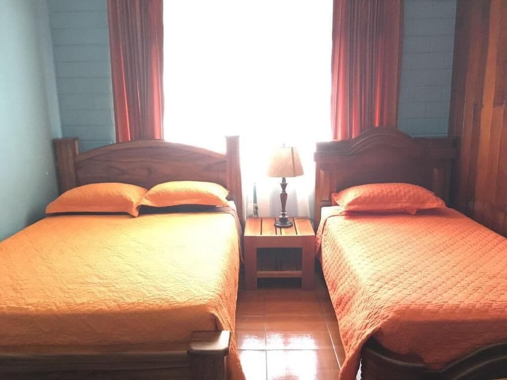 A room with two beds, each with a wooden headboard, a nightstand between them, and a lamp on the nightstand.