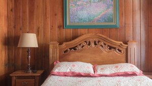 A wooden-paneled room with a bed, a nightstand, a lamp, and a framed painting on the wall. - Casa Hotel Sura (San José)