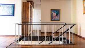 A staircase with a metal railing, wooden paneling on the walls, and artwork on the walls. - Casa Hotel Sura (San José)